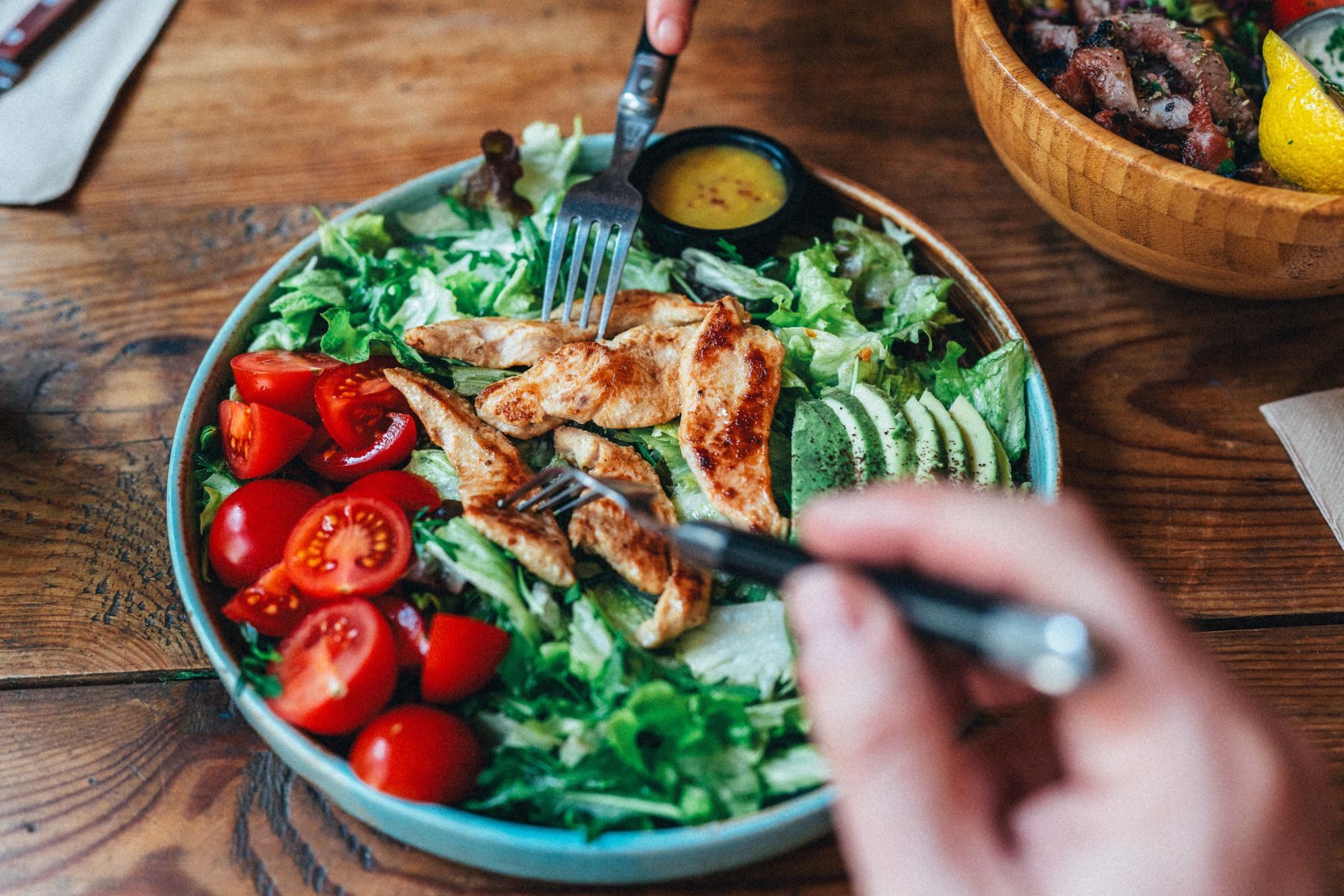 A fresh salad with chicken, avocado, tomatoes, lettuce and a dressing
