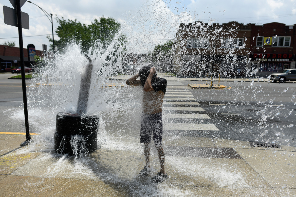 A person cools off with water from an open fire hydrant during a heat wave