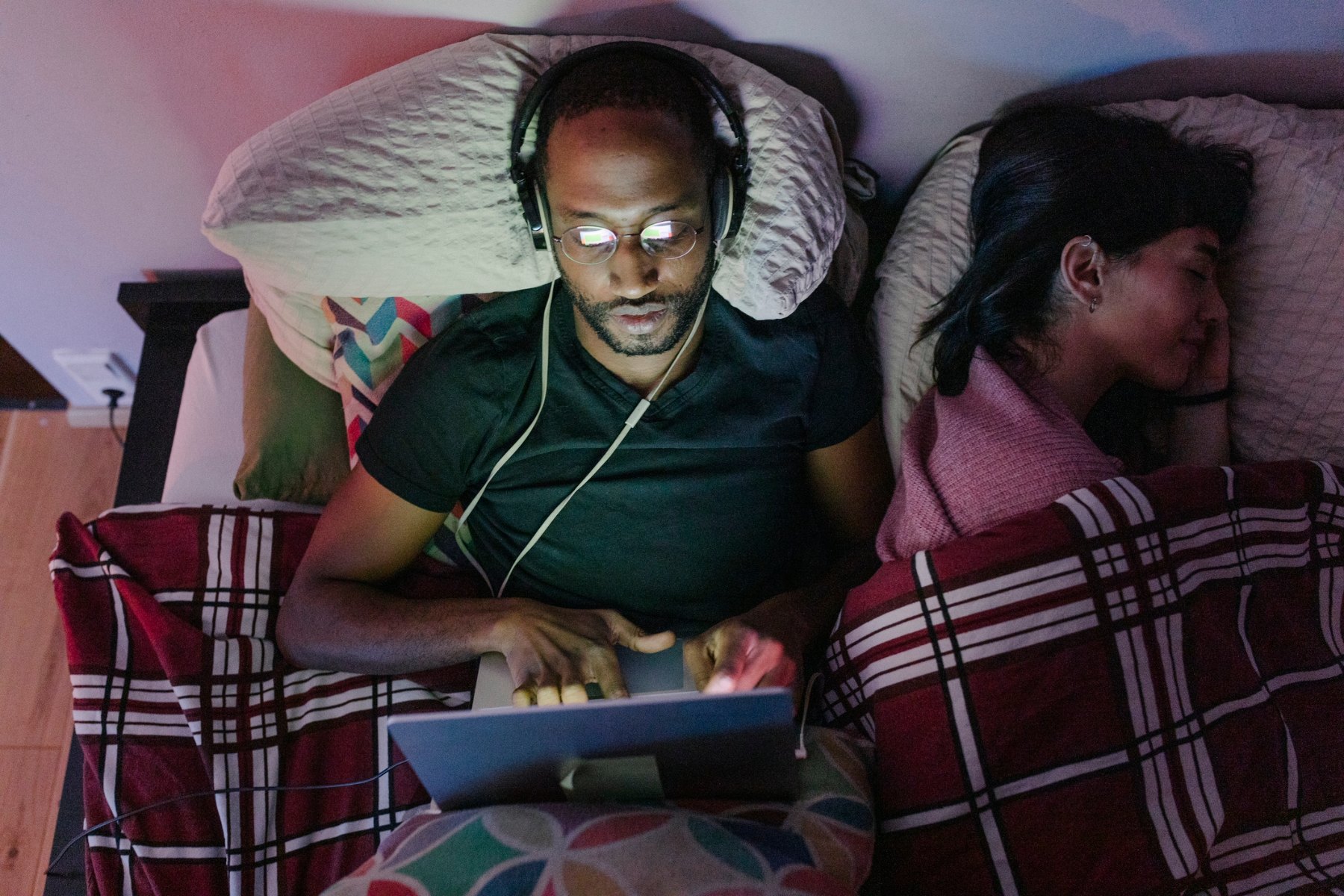 Man in bed on laptop with wife next to him