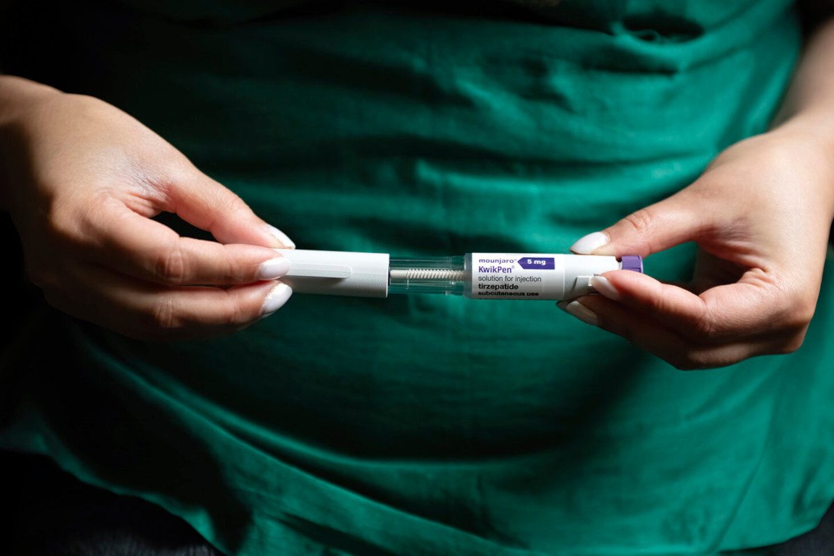 Close up photo of someone holding a Mounjaro injector pen up to the camera in front of their stomach