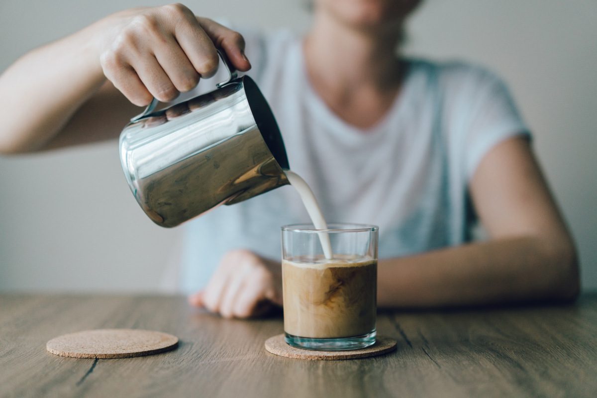 Photo of a person pouring cream/milk into a glass of coffee
