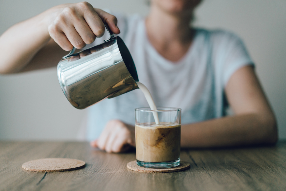 Photo of a person pouring cream/milk into a glass of coffee