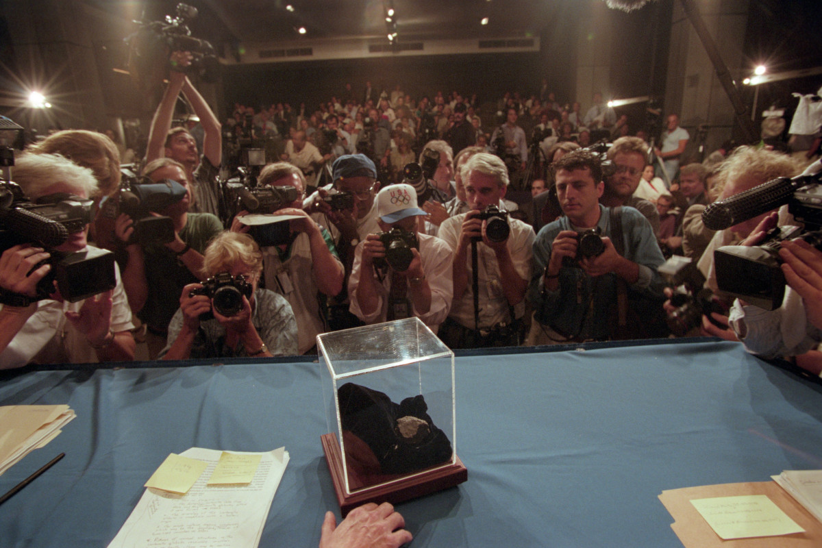Photo of the Allan Hills 84001 Martian meteorite NASA press conference, dozens of people are crowding to see the meteorite piece in a box on a table