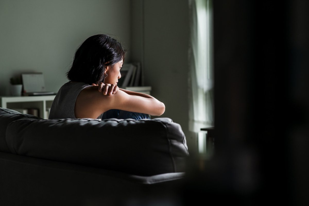 Young woman sitting on sofa at home feeling sad, tired and worried, suffering depression in mental health