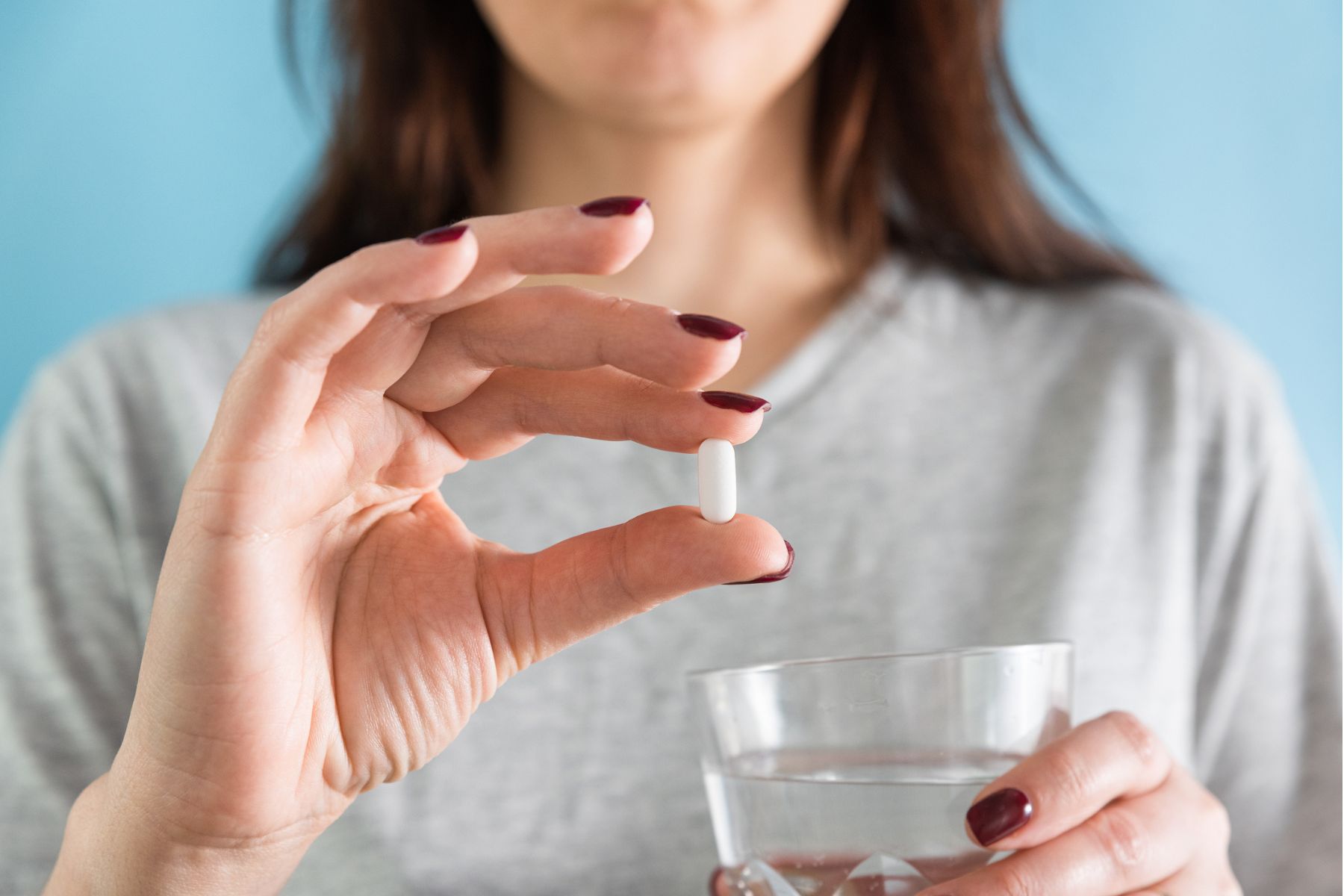 A woman holds a white statin pill and a glass of water
