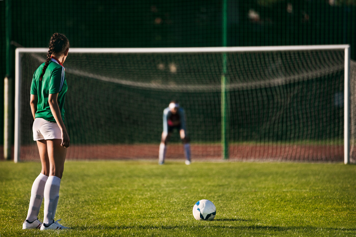 Photo of a football player about to take a penalty. The goalkeeper waits in the background