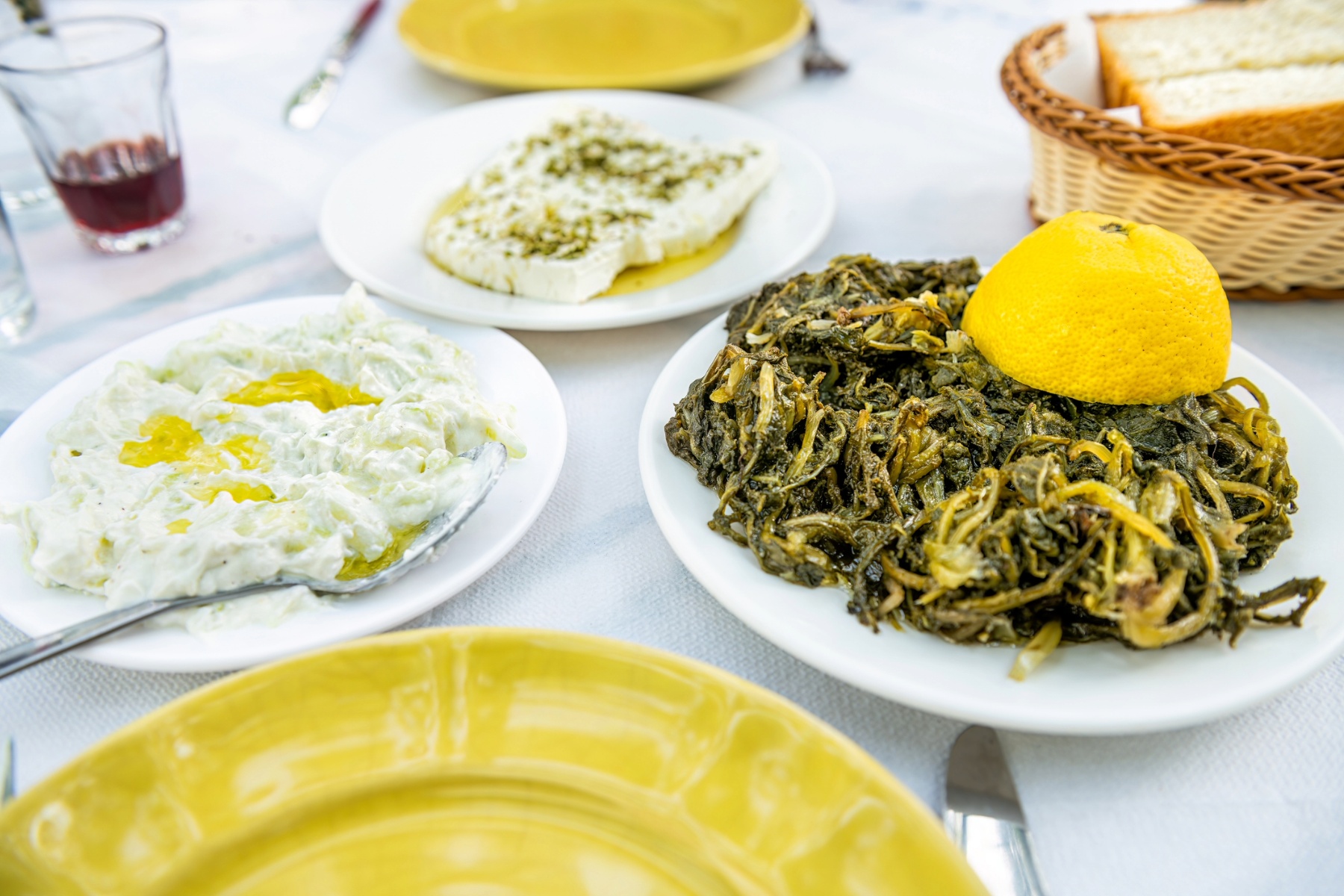 Table of Ikarian dishes – wild greens, tzatziki, feta and bread – with a glass of red wine.