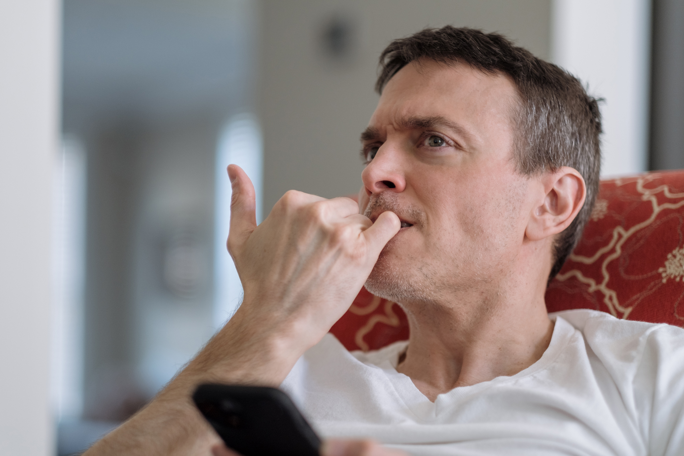 Close-up of mid adult man sitting in chair at home nervously biting his nails