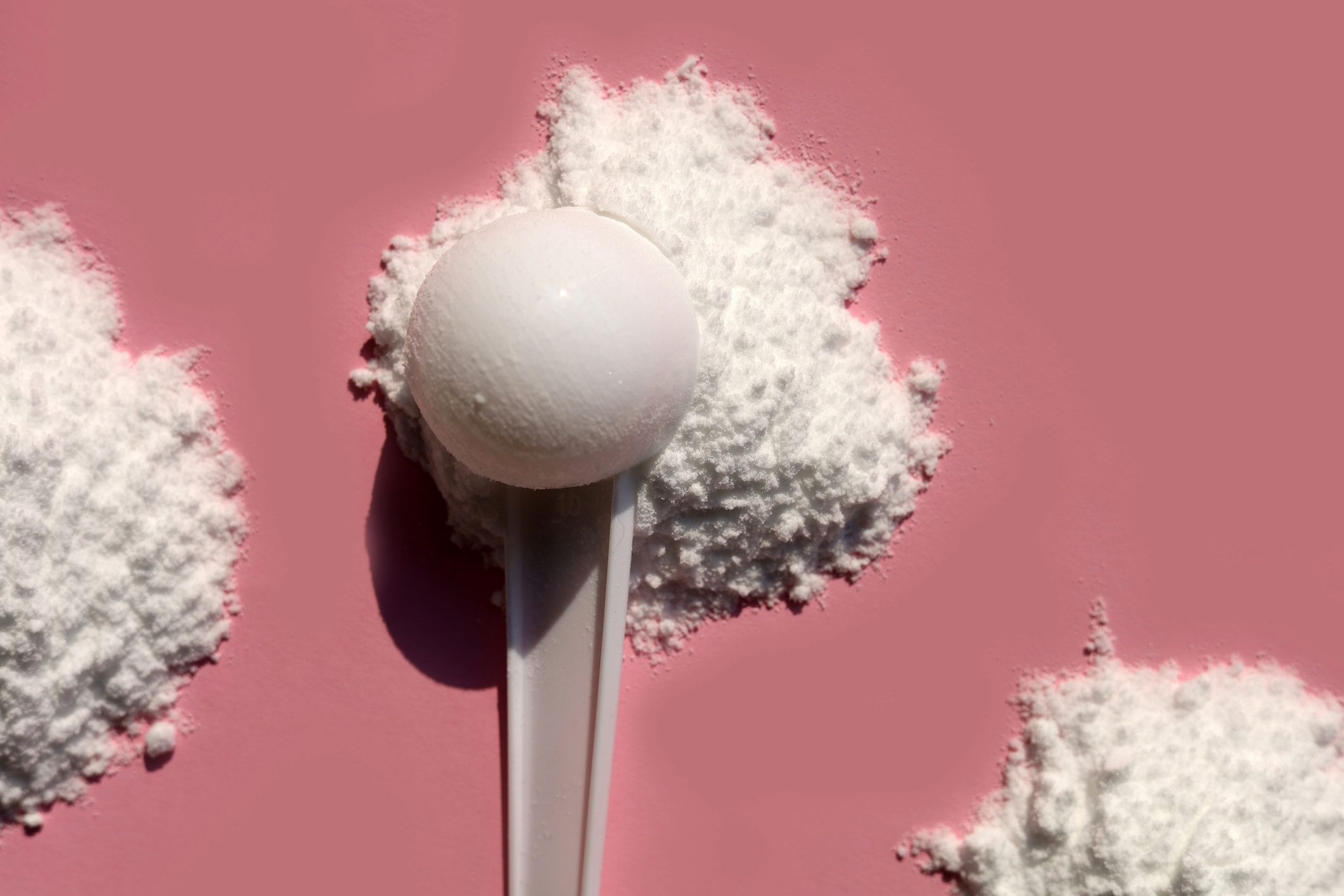 Scoops of creatine on dark pink background.