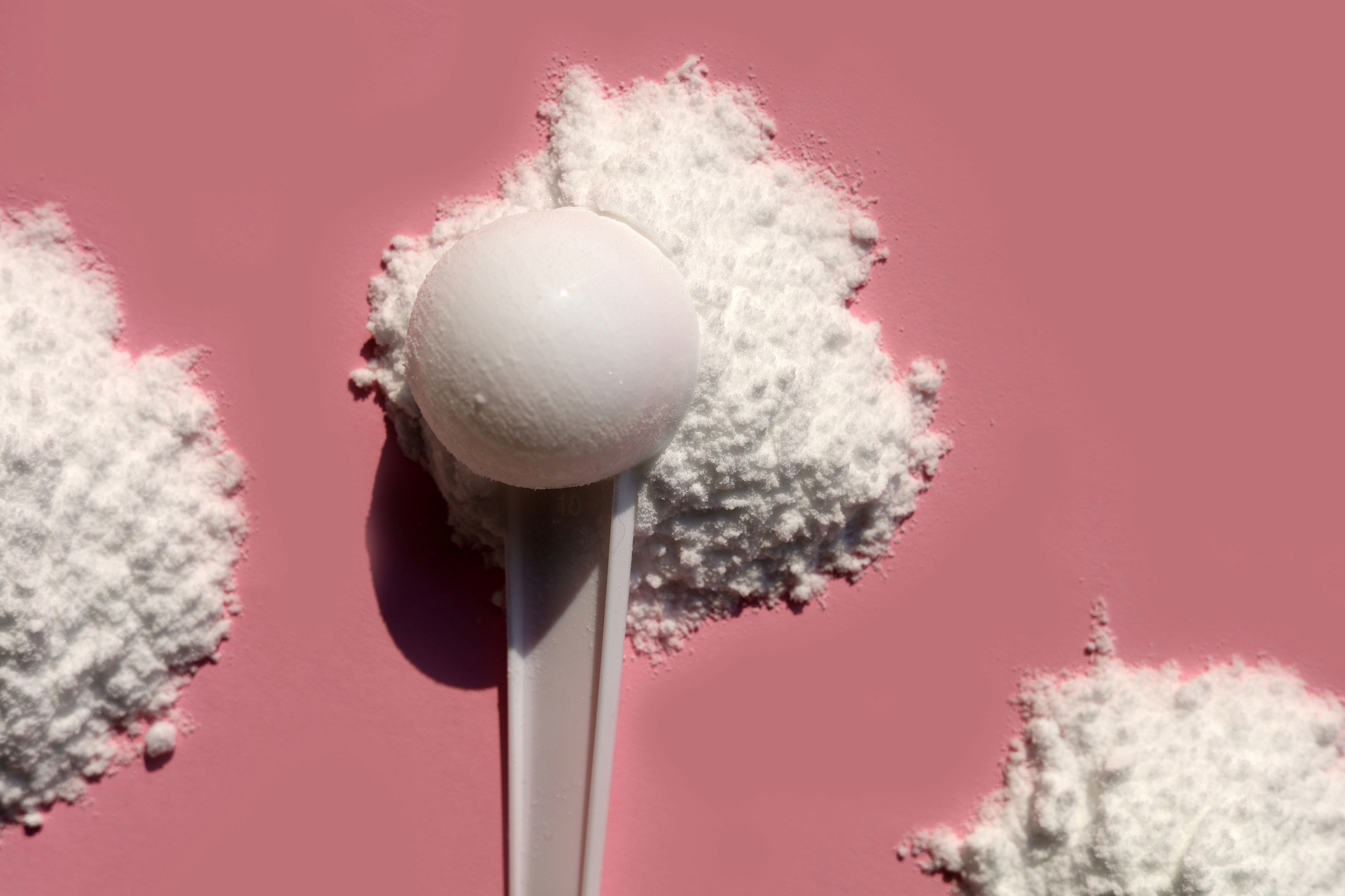 Scoops of creatine on dark pink background.
