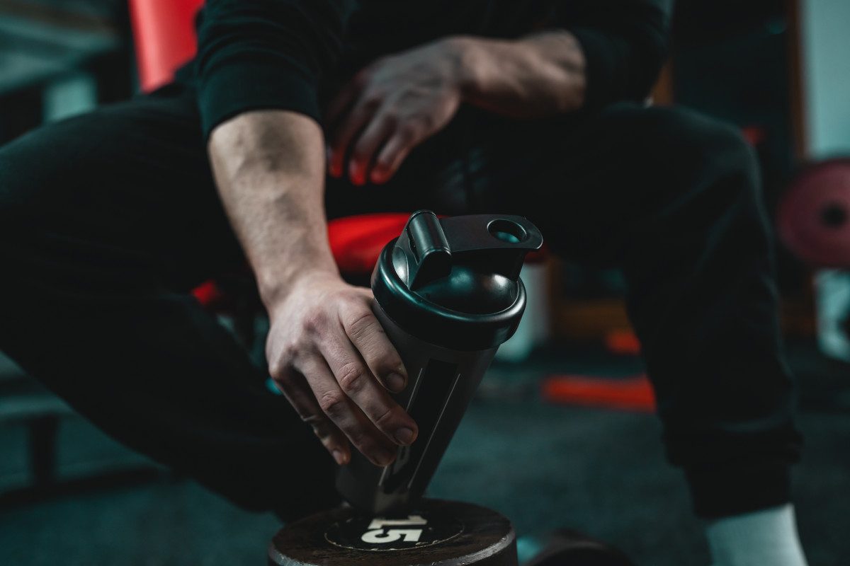 Close up of a person sat down in a gym holding a black reusable water bottle.