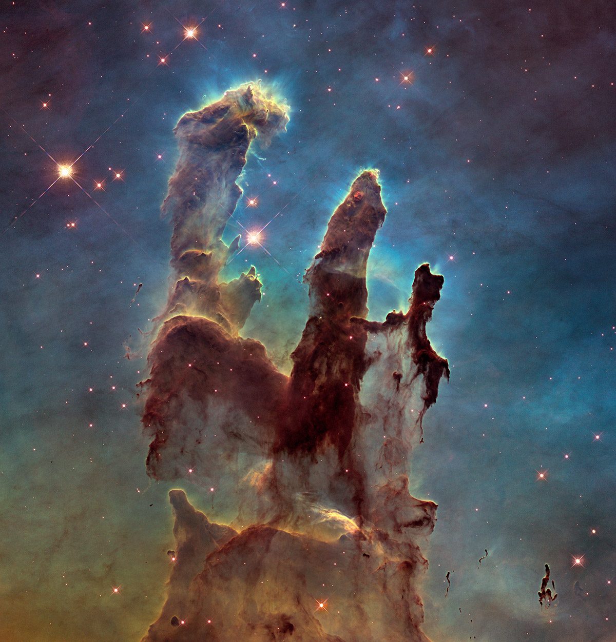 Hubble image showing three tall pillars of dark interstellar gas and dust, glowing at the edges under intense starlight, rising from a colourful nebula against a star‑filled background.