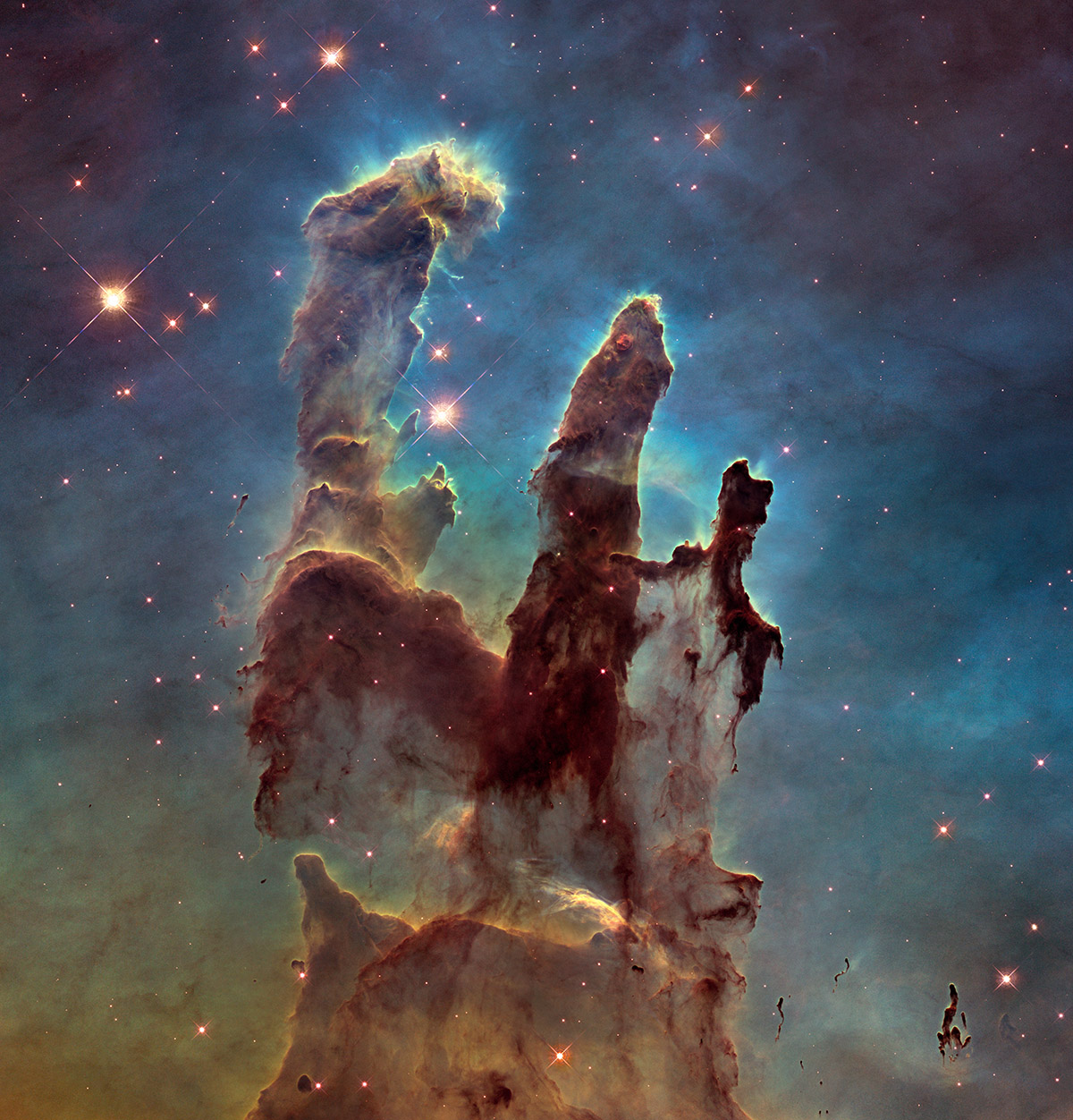Hubble image showing three tall pillars of dark interstellar gas and dust, glowing at the edges under intense starlight, rising from a colourful nebula against a star‑filled background.