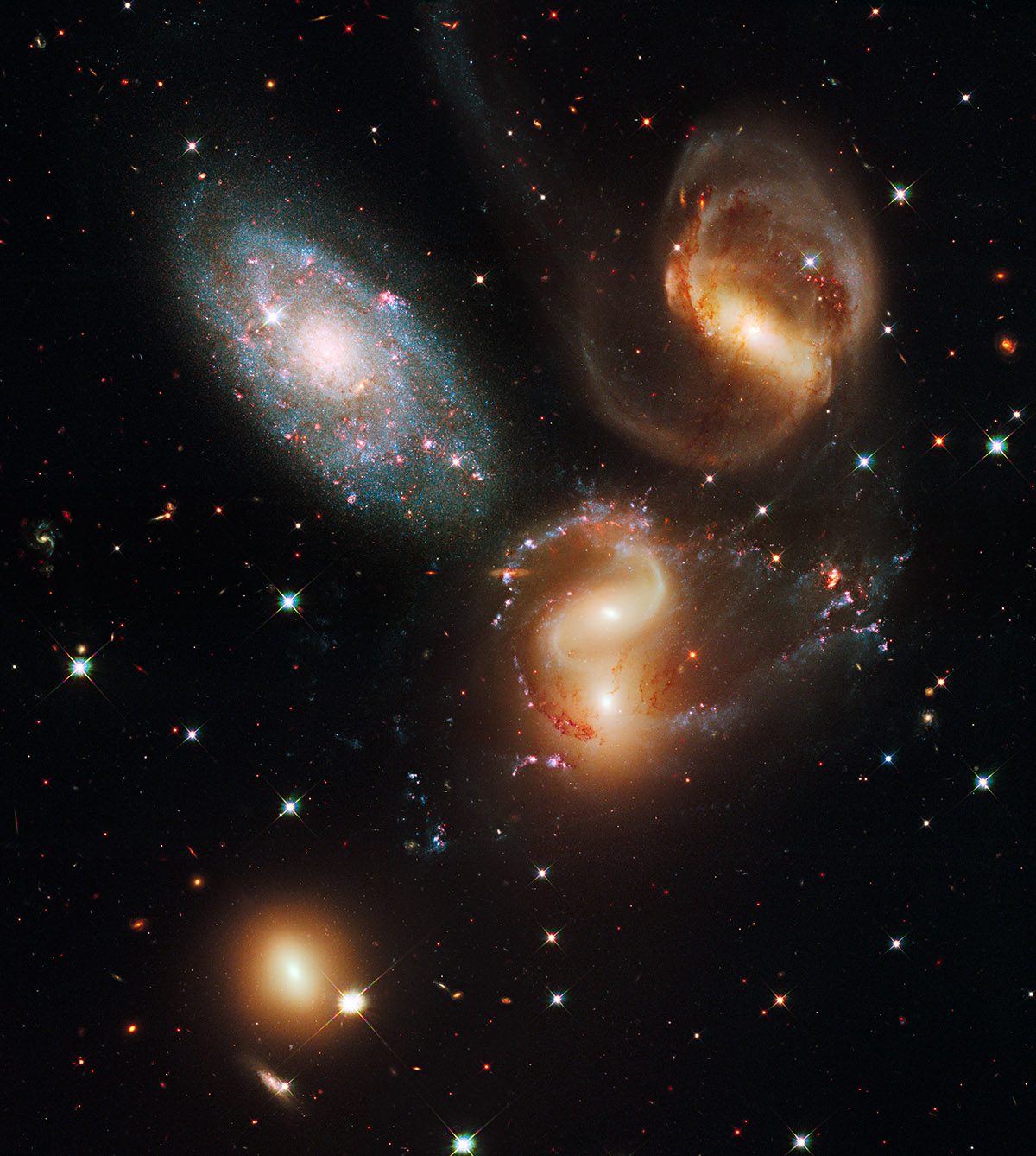 Hubble image showing a small group of galaxies, including two bright spiral galaxies with distorted arms and glowing regions, set against a dark background filled with scattered stars.