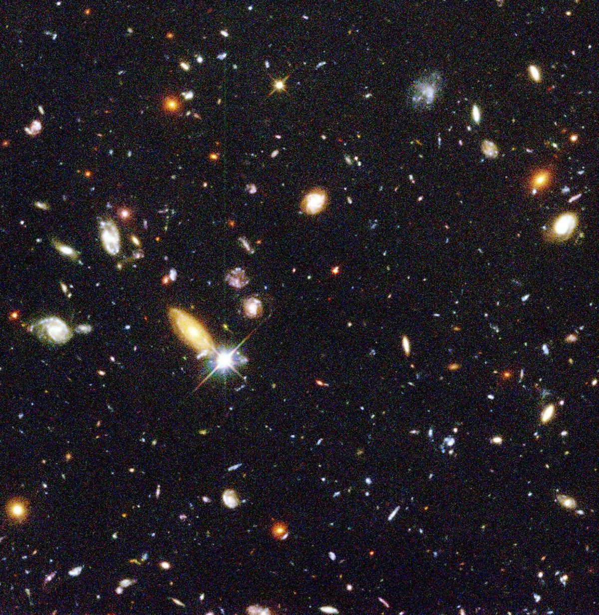 Hubble image showing thousands of distant galaxies, appearing as small dots and smudges in many colours, filling a tiny patch of deep space.