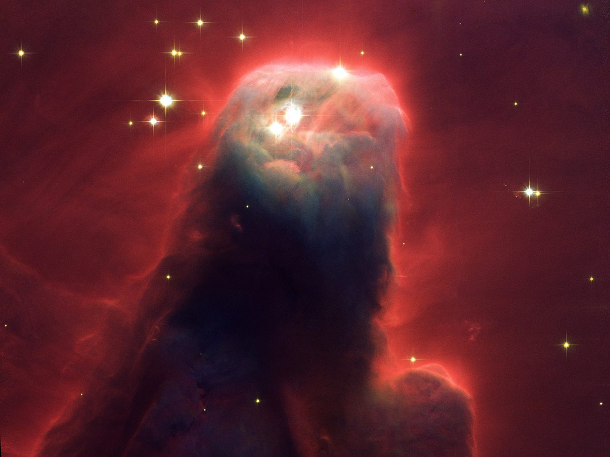 A conical cloud of dust is surrounded by a red glow with small glowing stars at the tip and surrounding it.