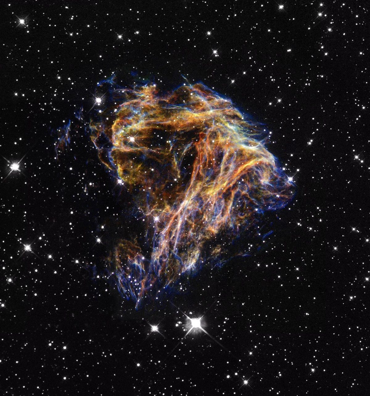 Fine, yellow and blue thread-like filaments of glowing gas spreading outward like sparks against a dark background of space.