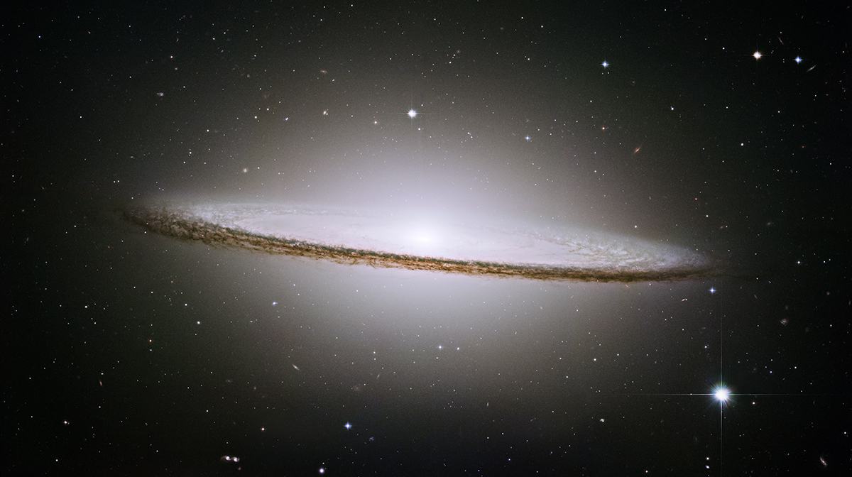 An edge‑on galaxy with a bright central bulge and a dark dust band forming a wide, flat disc against a black background of space.