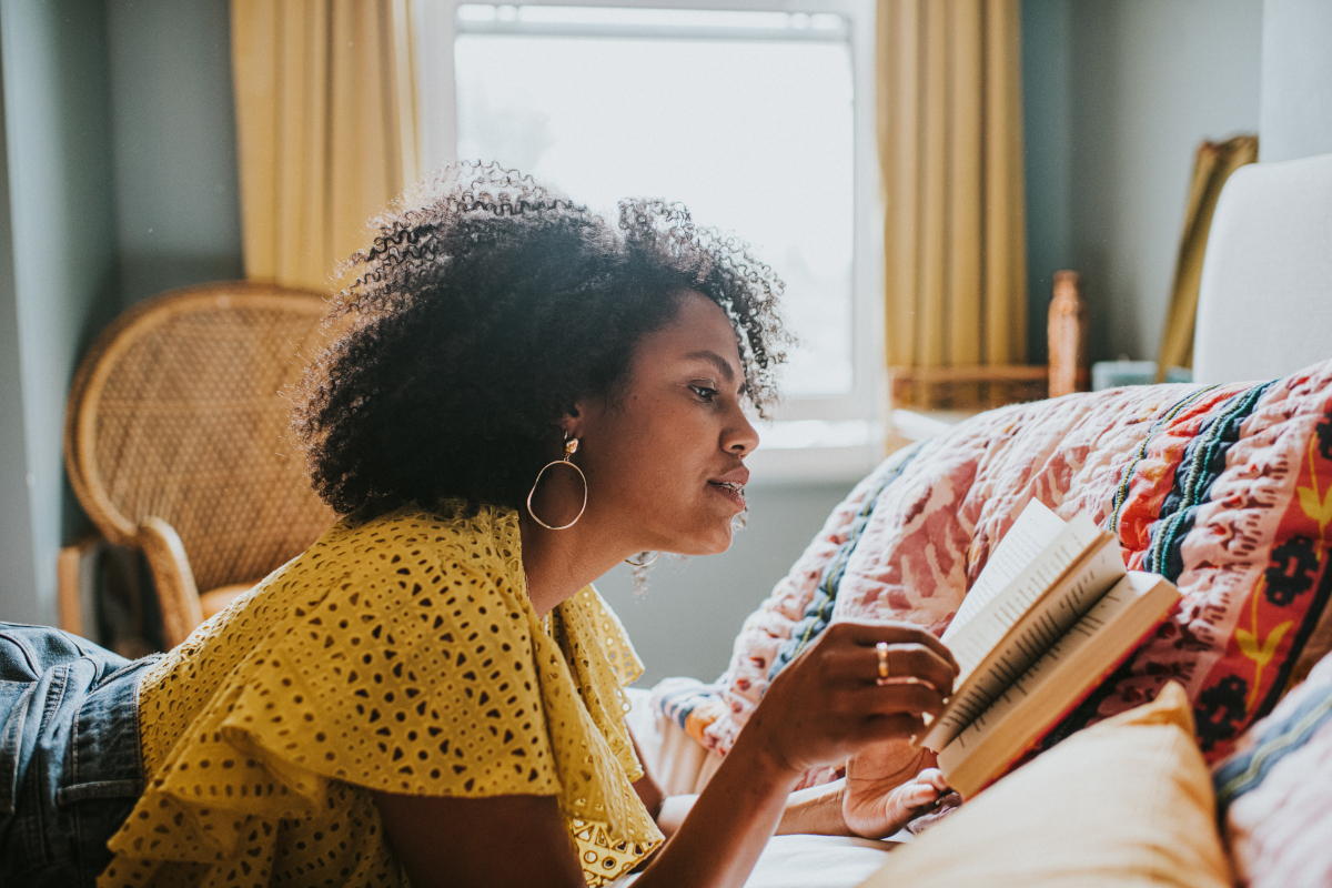 A person lying down on their stomach reading a book in a well-lit cosy room.