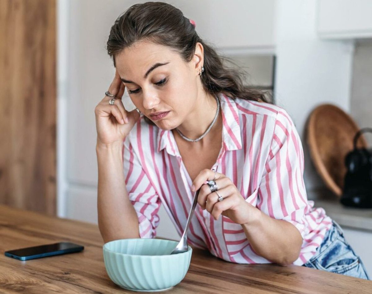 A person sat at a table, looking at a bowl of food with a face of disgust