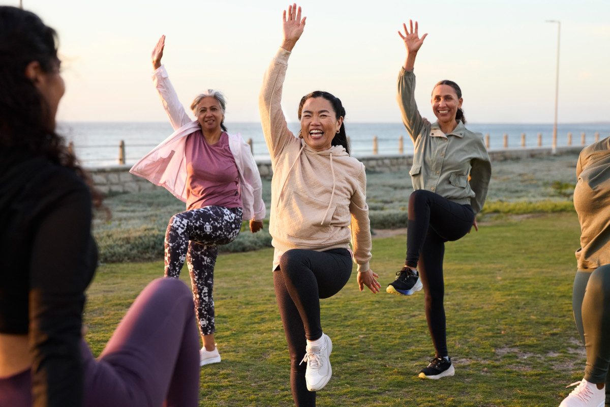 Happy mature woman exercising with friends. Active people are following fitness instructor, all standing on one leg