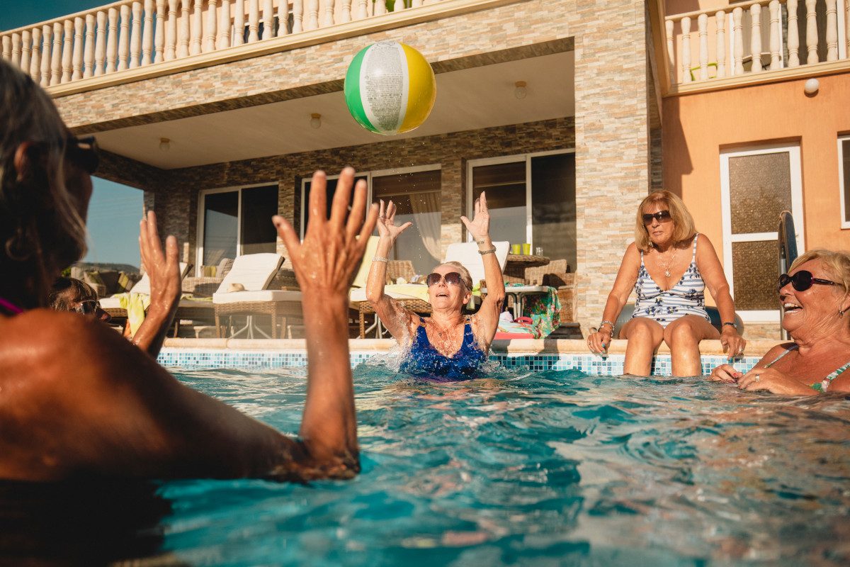 Group of senior female friends having fun. They are playing with an inflatable ball in the pool on holiday.