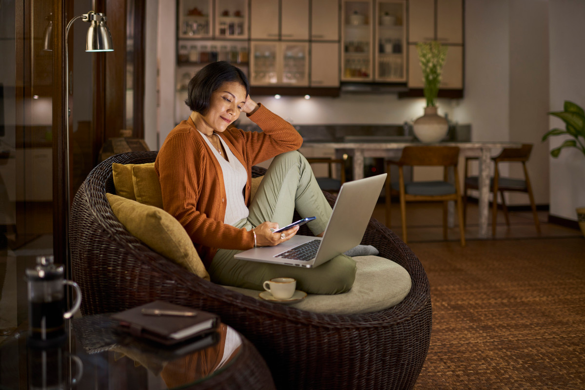 Woman sat smiling at her phone, laptop on and open too on her lap