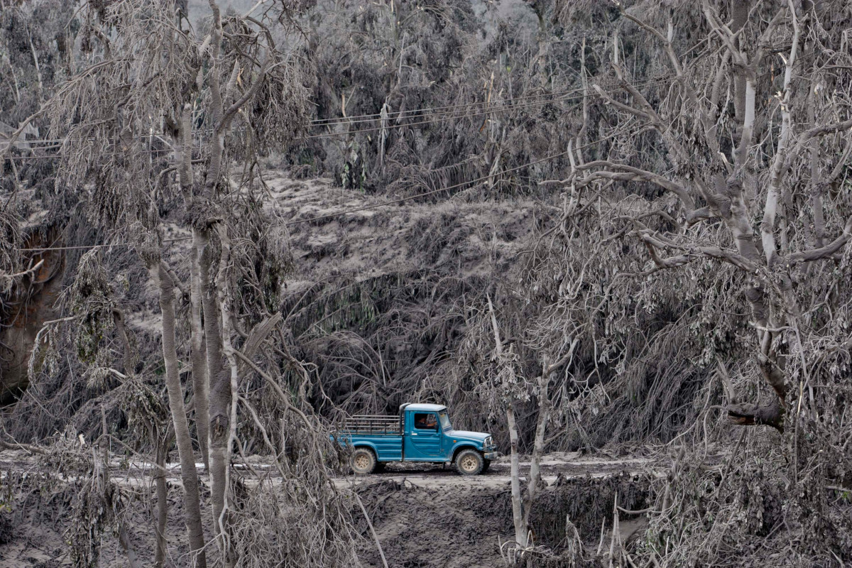 A single blue pickup truck drives along a road through an ash-covered devastated landscape