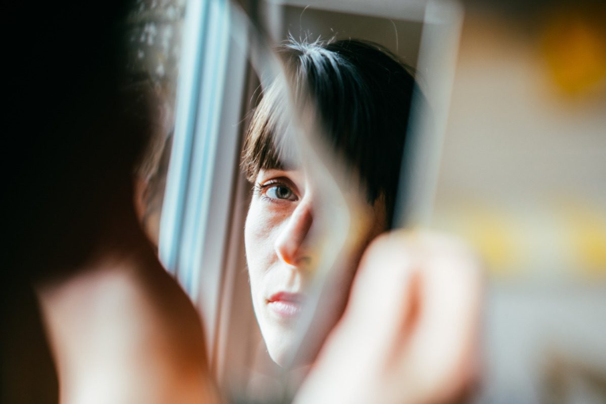 Close-up of a person looking into a mirror. They look a little forlorn
