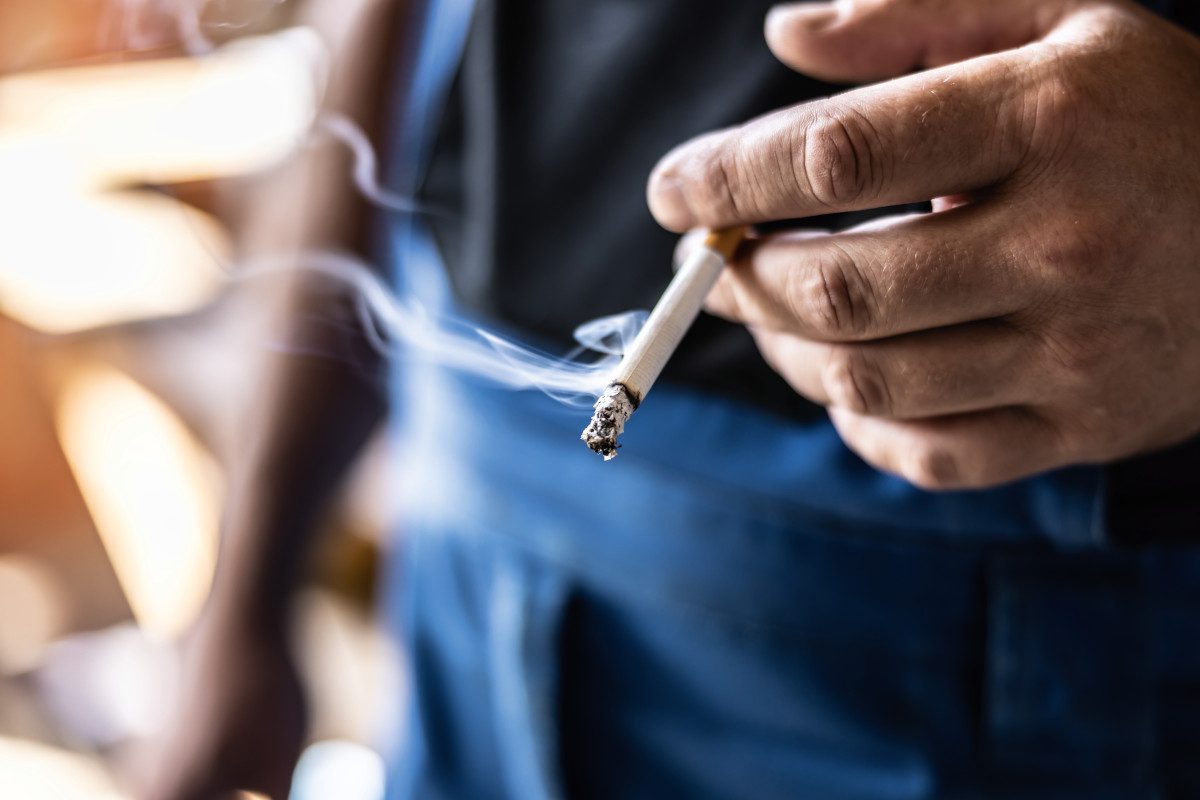 Detail of a man holding a lit cigarette in his hand