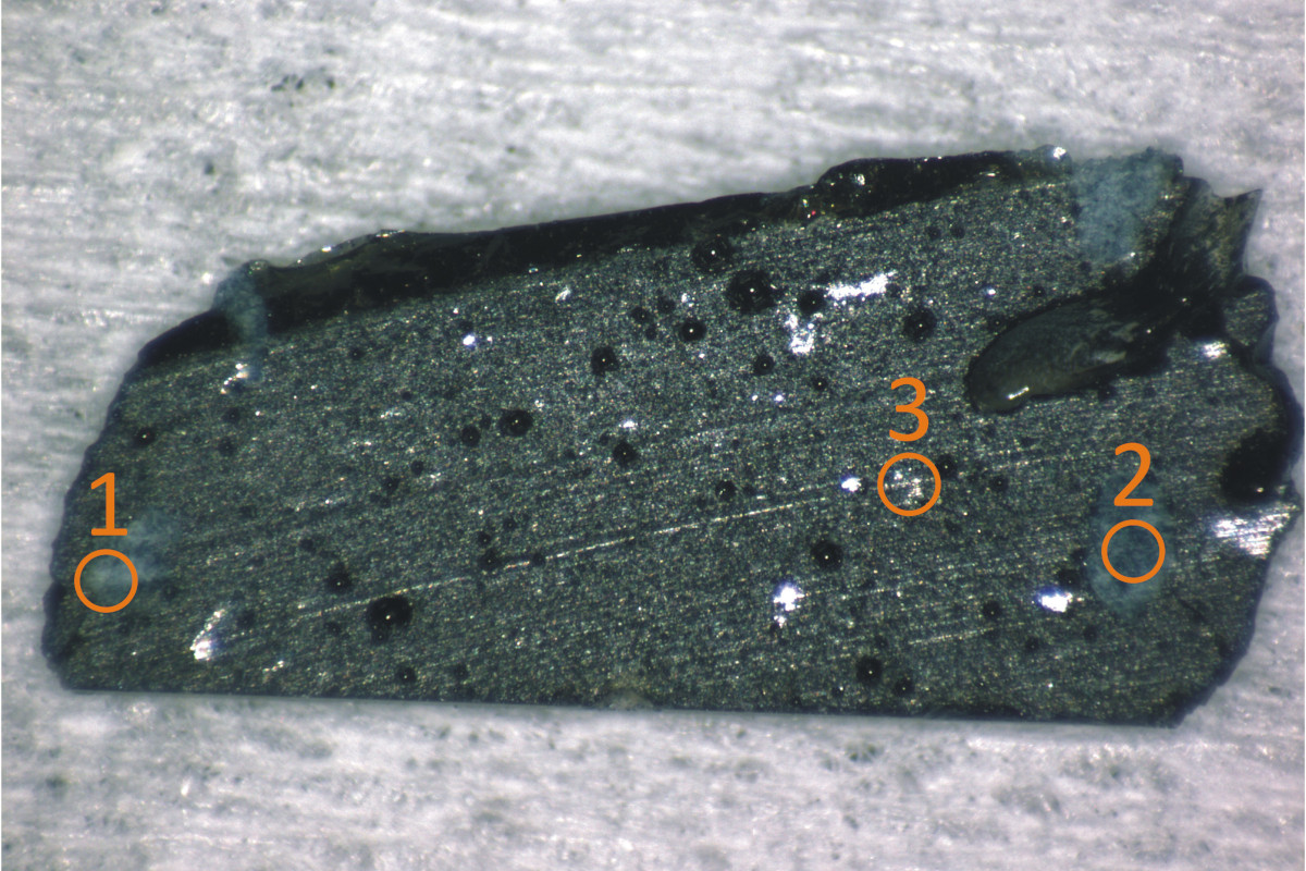 A small, 1mm-thick grey rectangular stone that is a lava sample from Chernobyl speckled with debris
