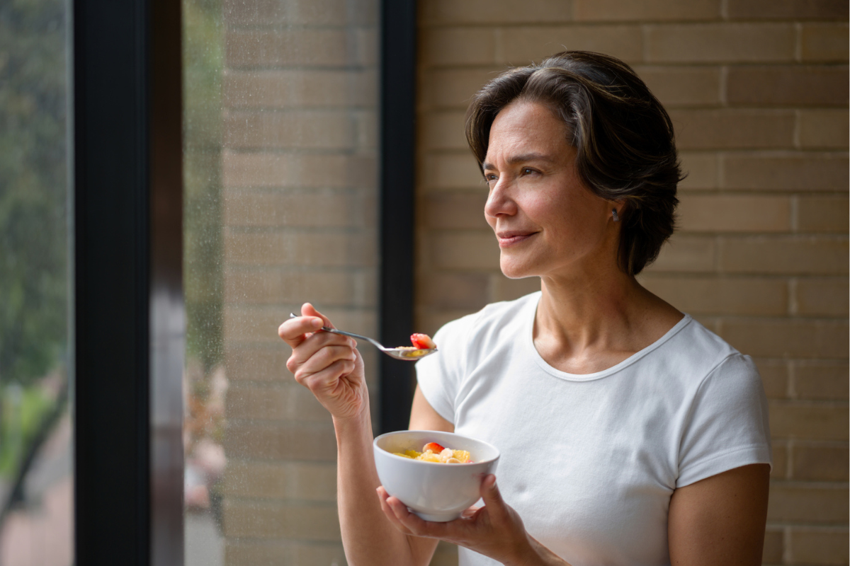 A woman eats fruit while looking out of the window.