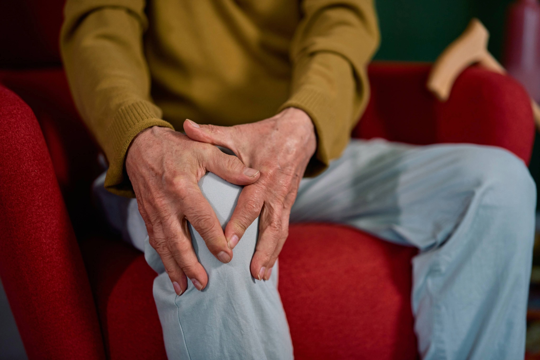 Mature person holding on to their knee with both hands, face not visible