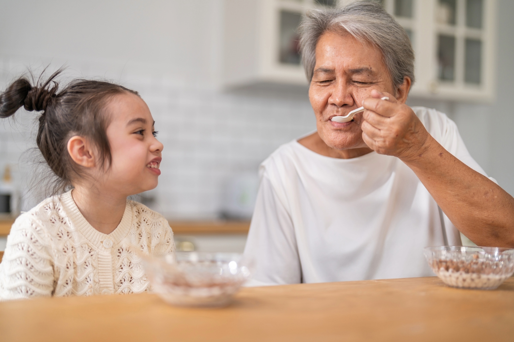 Older person spooning food into their own mouth while child looks at them, smiling