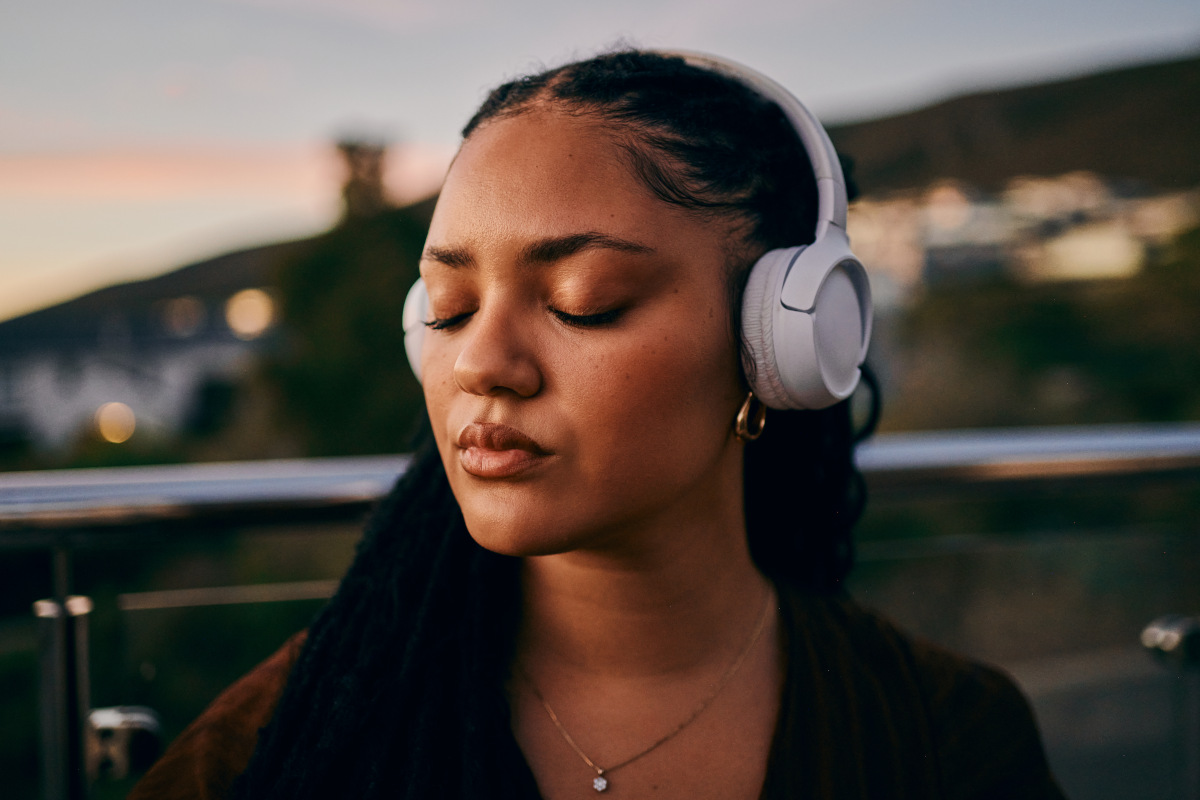 A young woman wearing headphones enjoys music outdoors during sunset, capturing a moment of calm and introspection