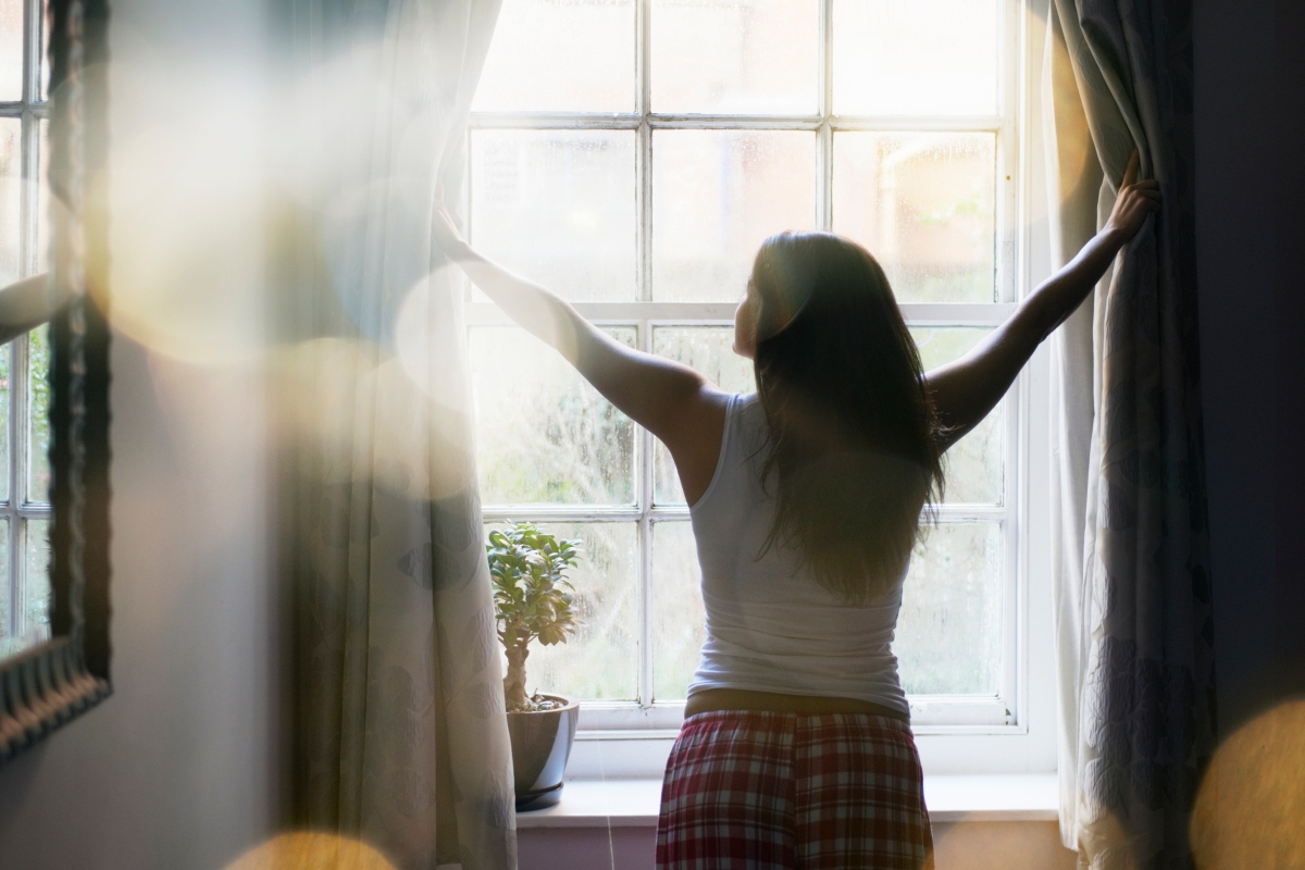 A woman waking up and opening the curtains right after she wakes up from sleeping
