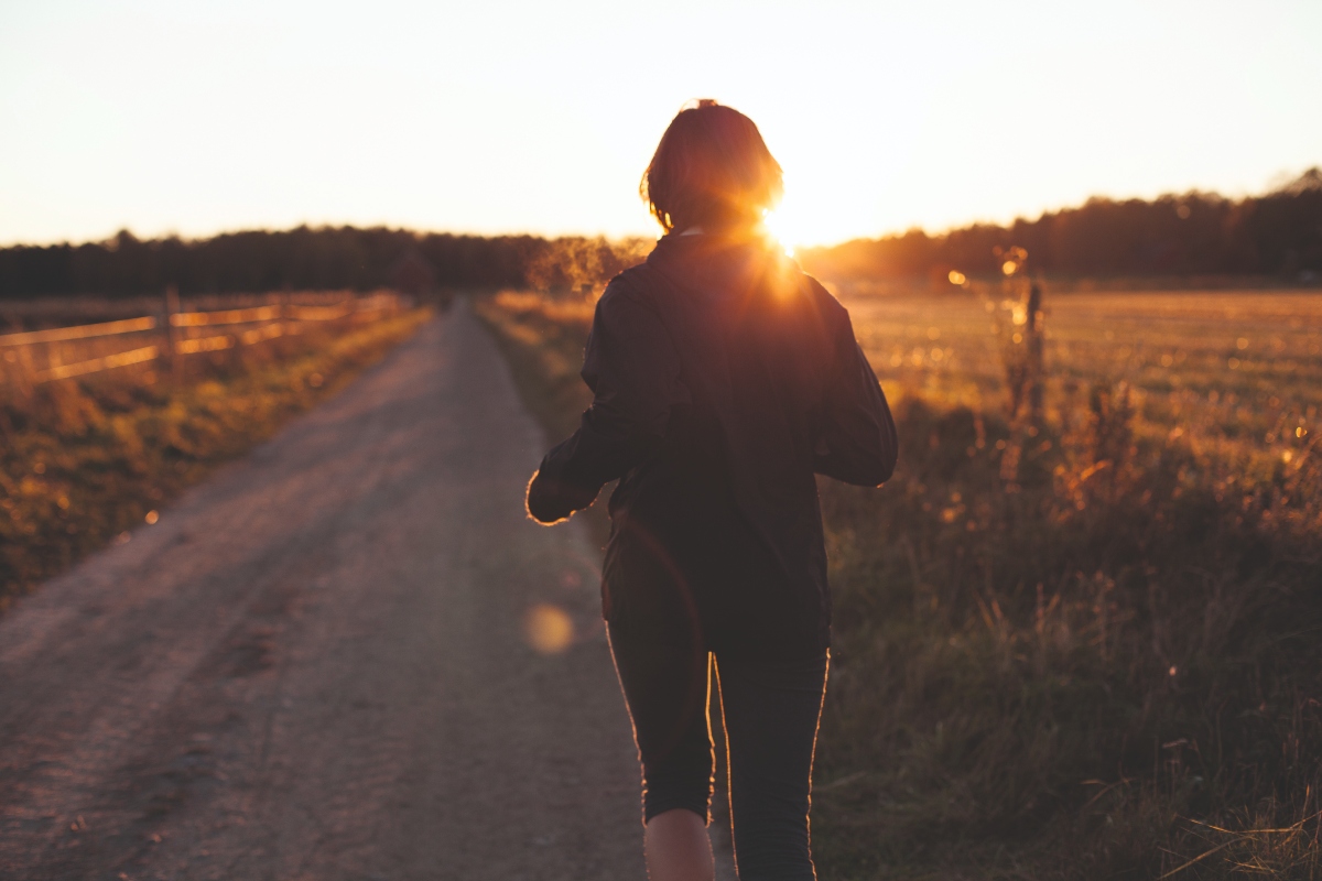 The back of a woman jogging on an empty road at sunrise