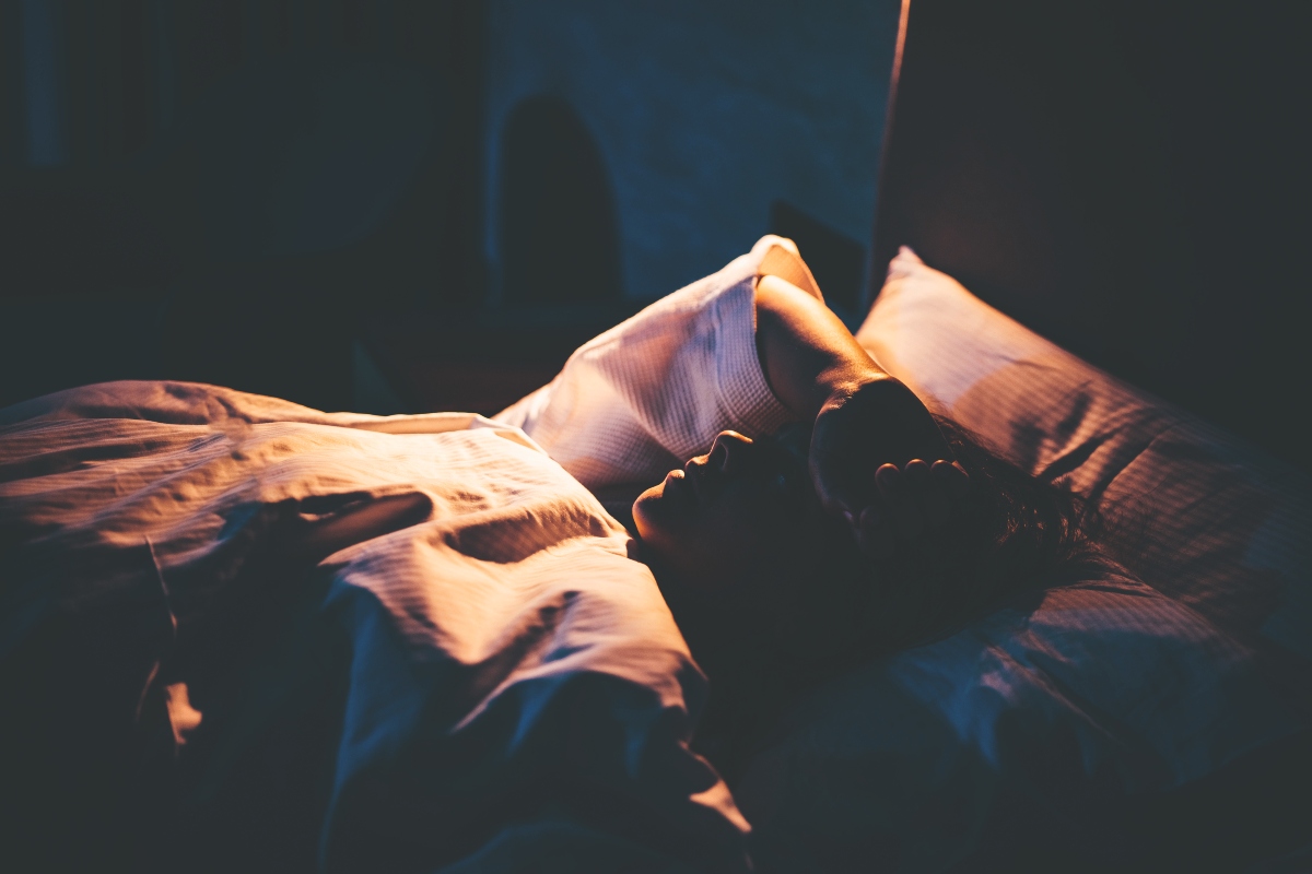 Woman with insomnia, lying on bed with hand on forehead.
