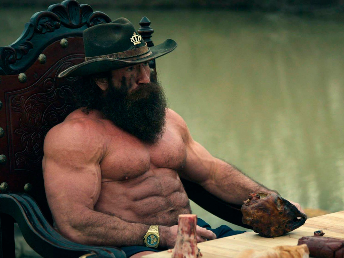 Photo of Brian Johnson, "the Liver King" sat topless on a throne with hunks of meat on a table in front of him