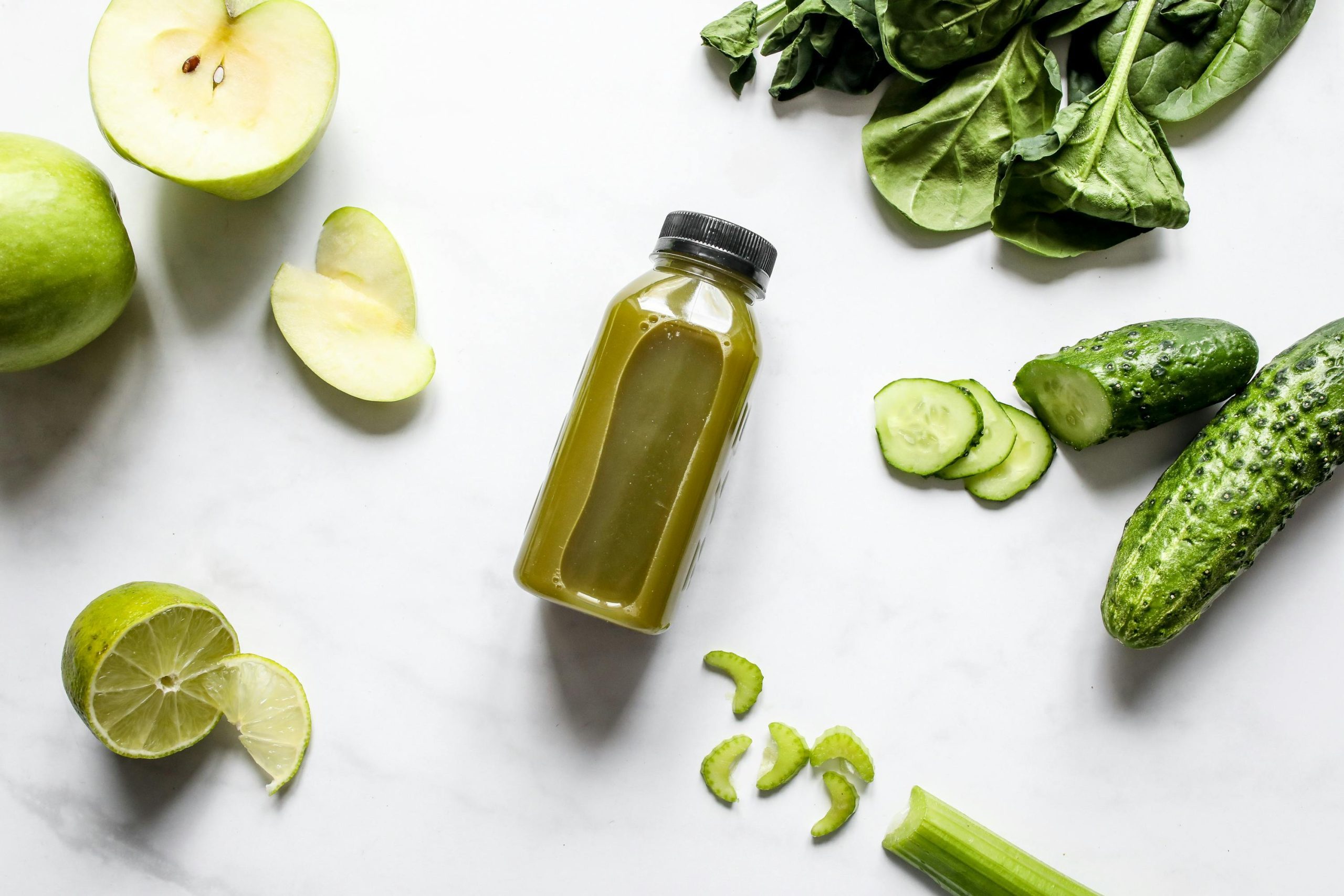 A bottle of green juice surrounding by sliced apples, cucumber and celery