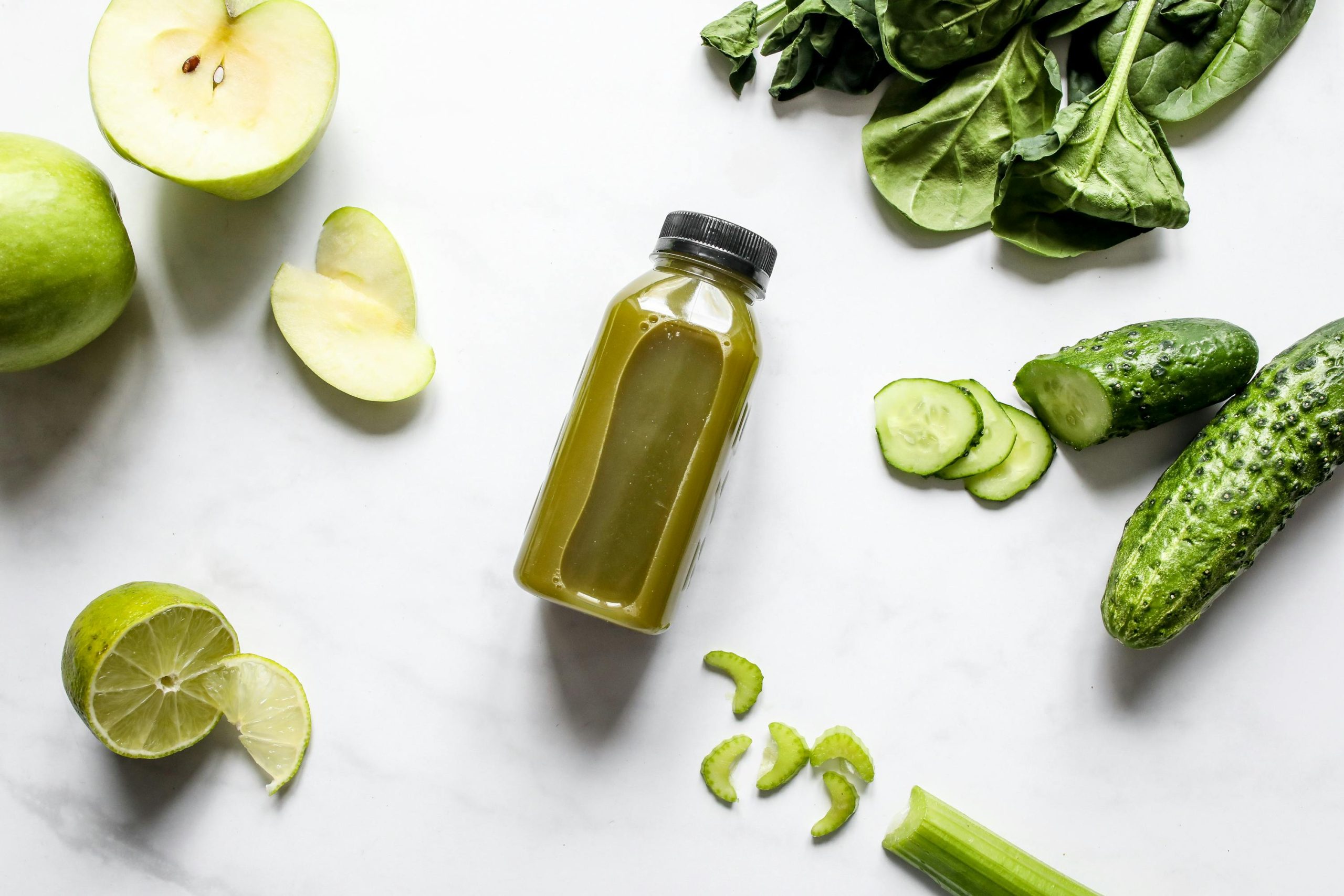 A bottle of green juice surrounding by sliced apples, cucumber and celery