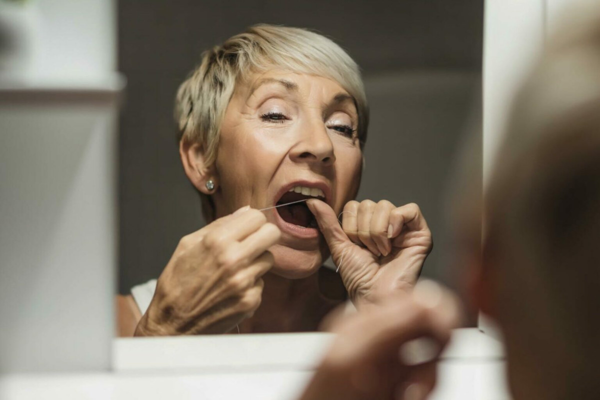 Photo of an elderly person flossing while looking in the mirror