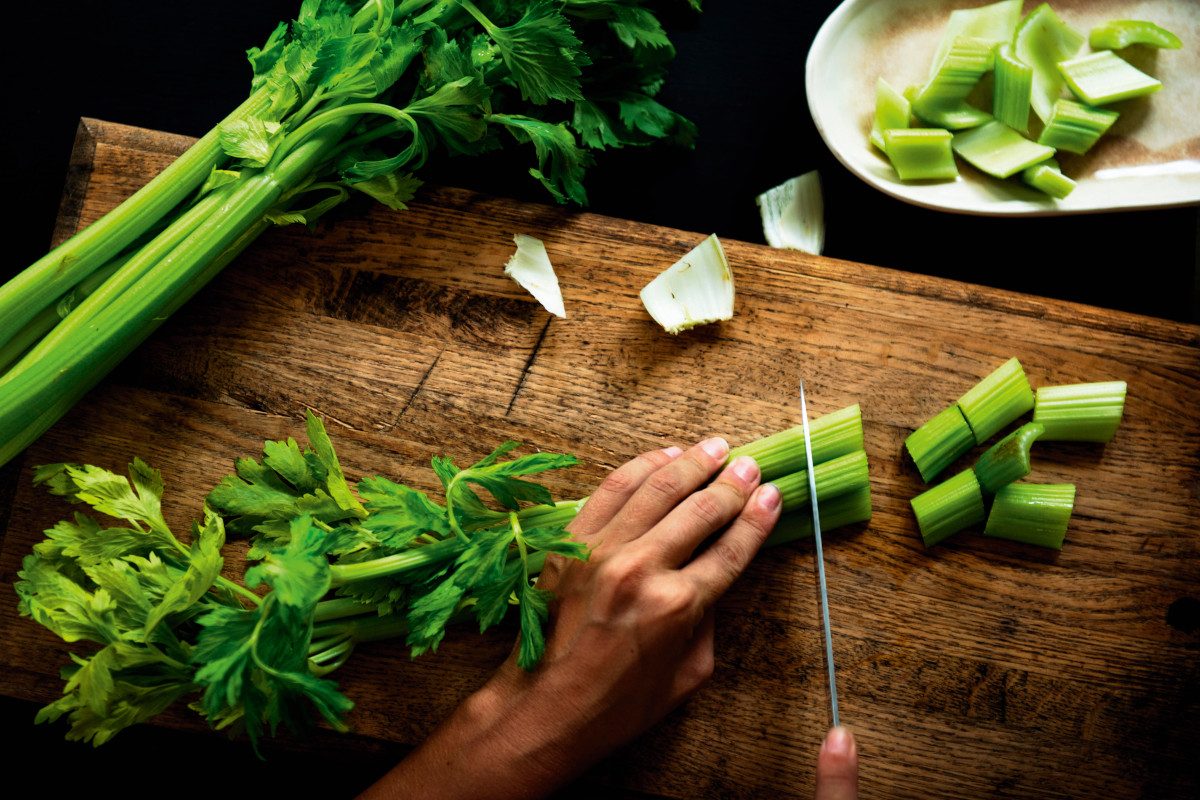 Aerial view of hands with knife cutting celery on wooden cut board