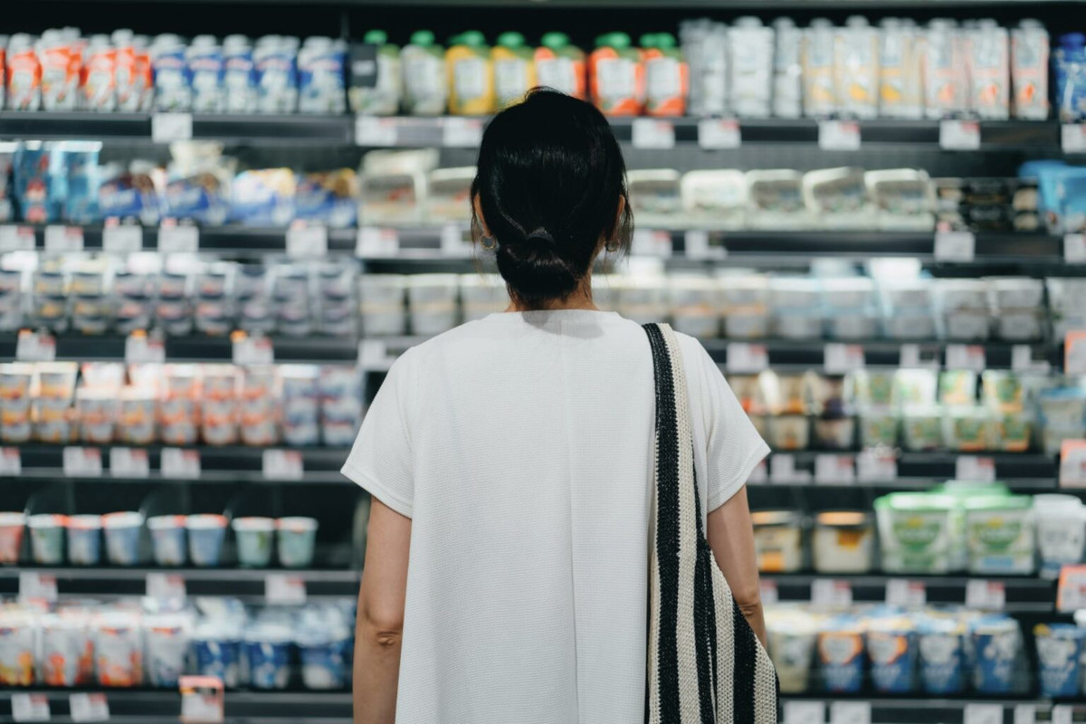 Photo of the back of a person, looking at the stocked shelves of a dairy aisle in a supermarket