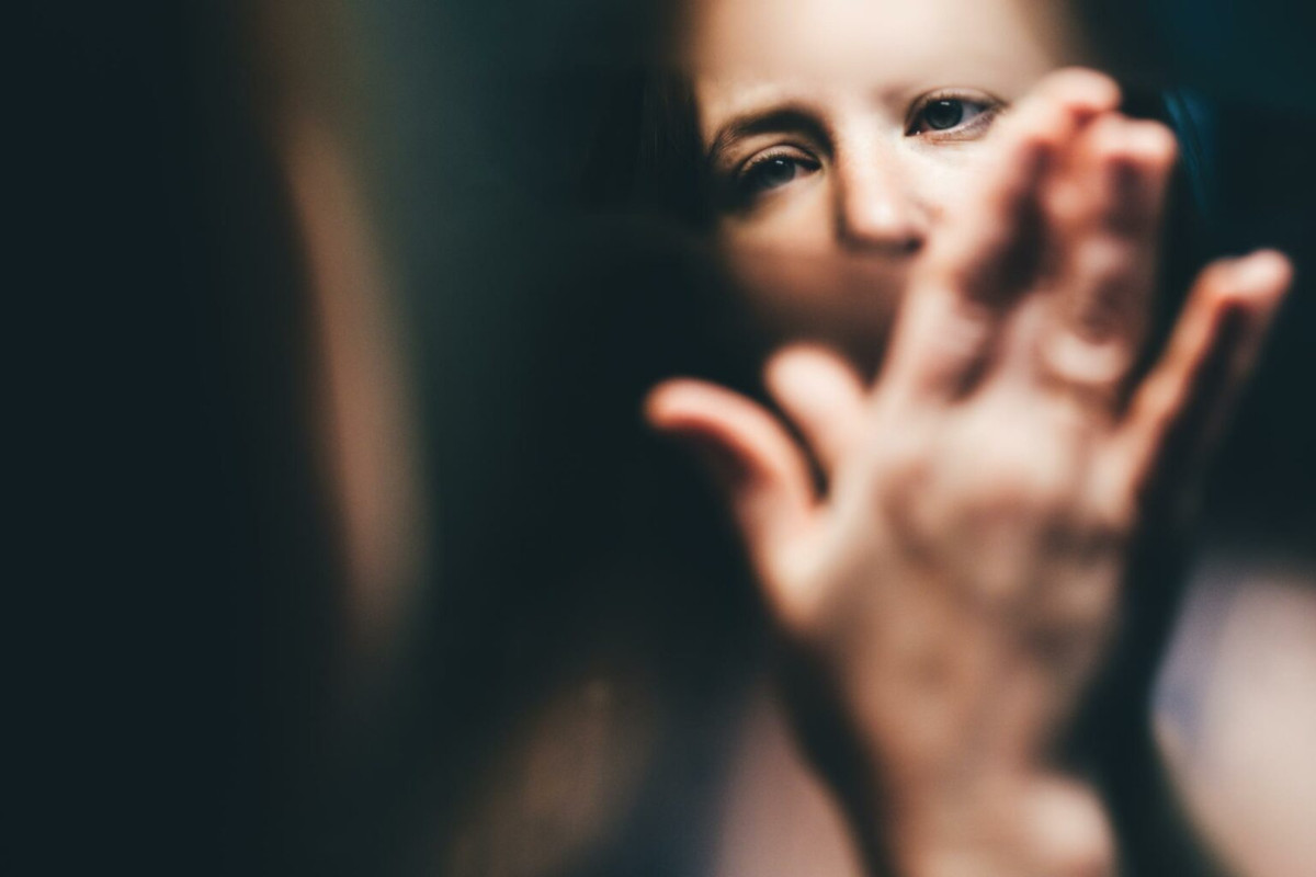 Photo of a person wiping away condensation from a mirror, you can see their eyes in focus in the reflection