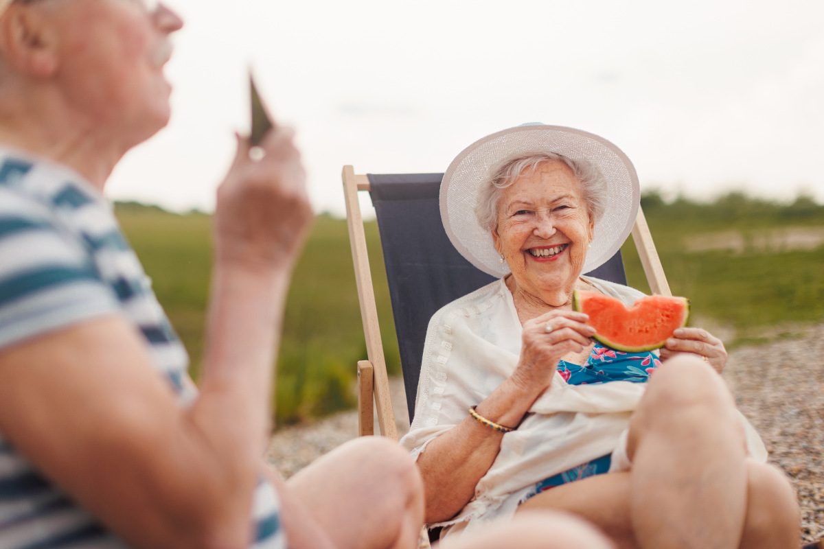 Senior couple enjoying summer time, sitting on deck chairs near water and eating melon.
