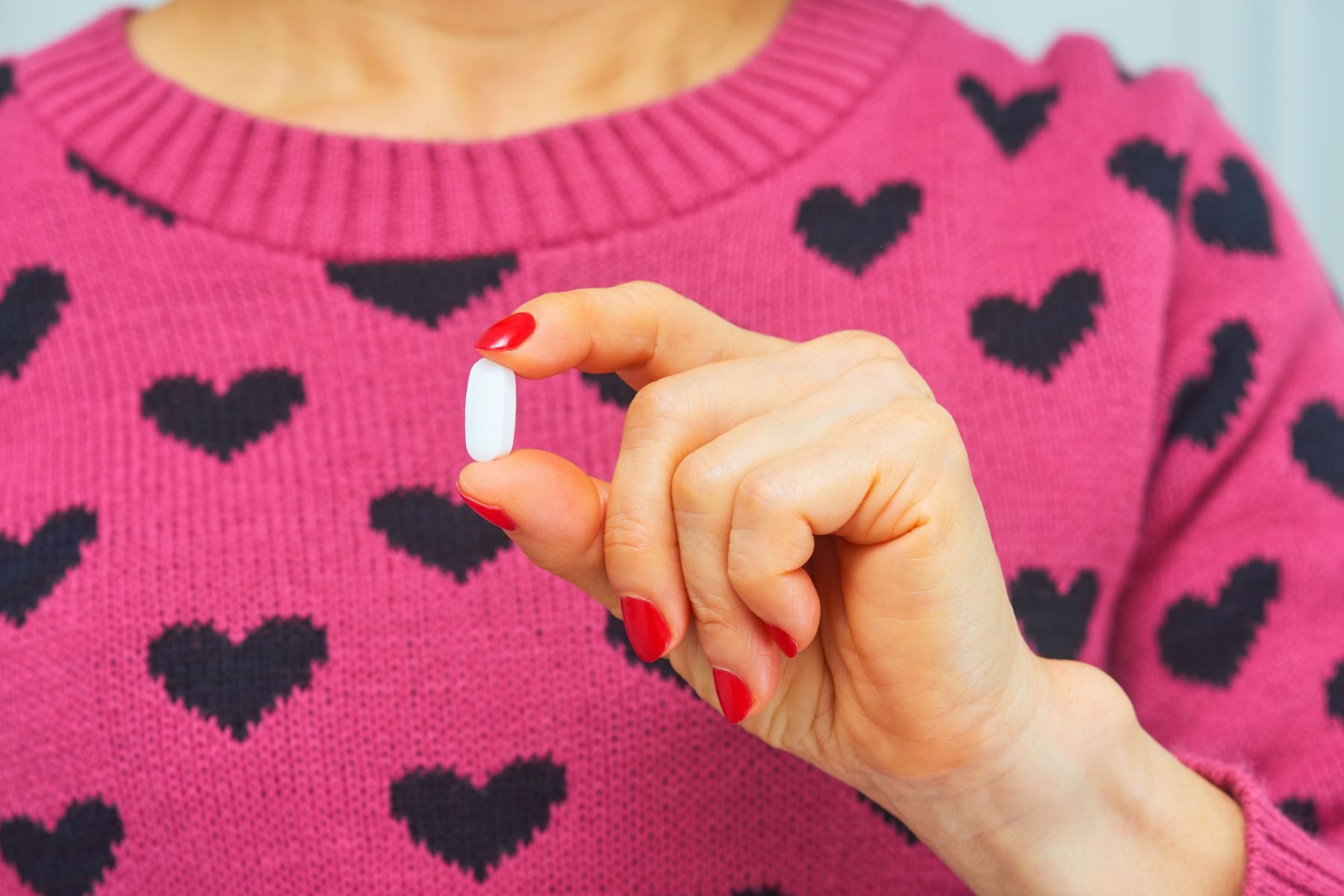 A woman in a heart-patterned jumper holds a pill