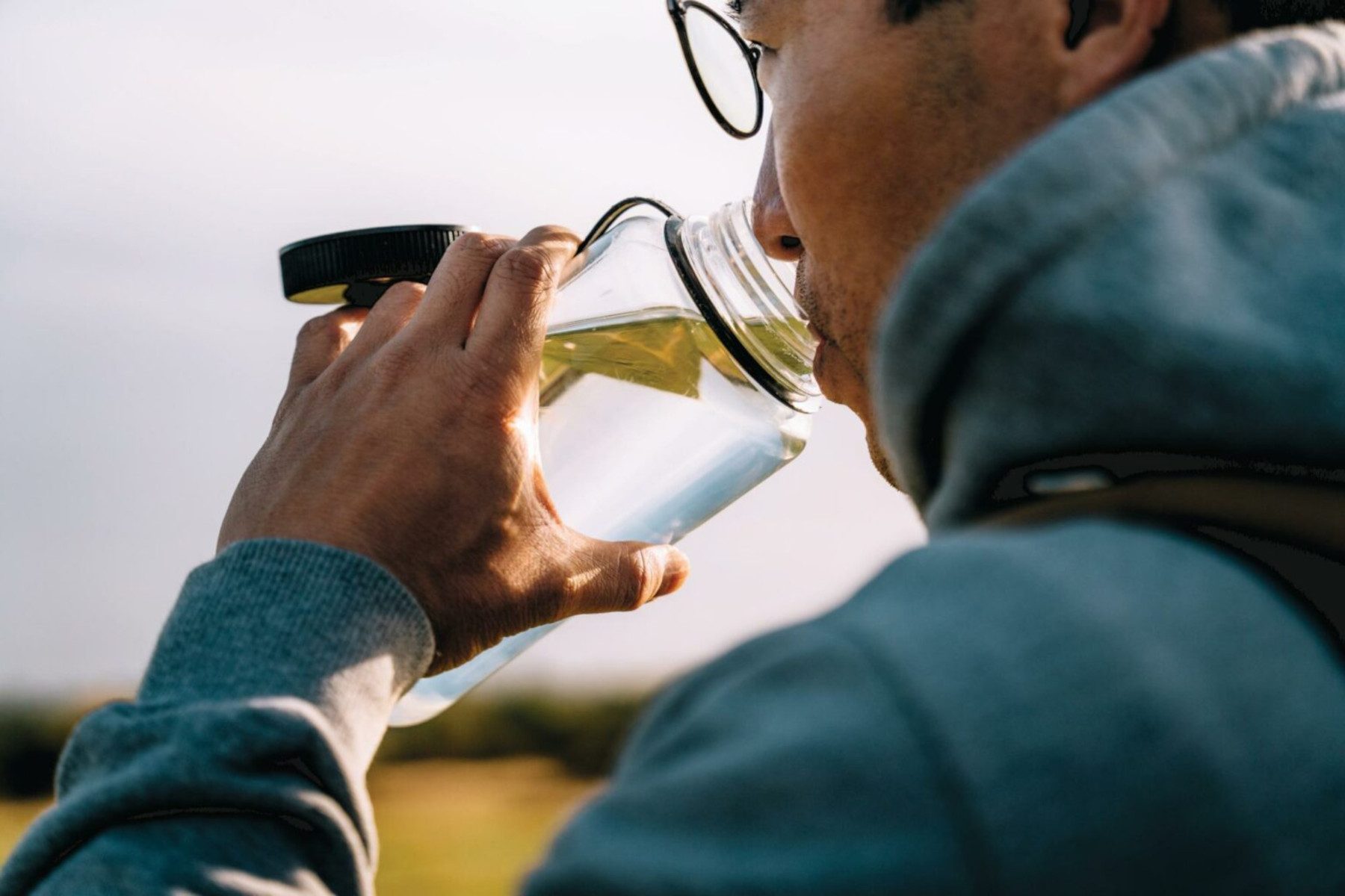 Photo of a person drinking water from a water bottle while on a walk