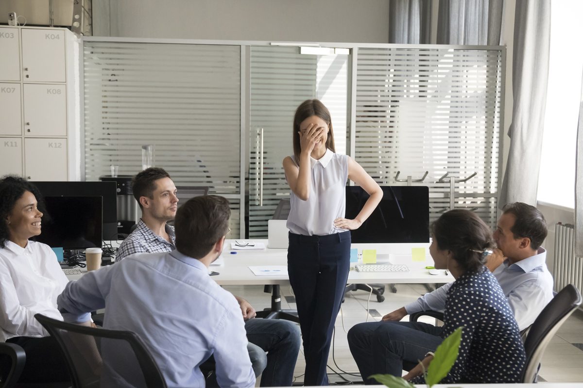 A person cringes while stood up in a meeting.