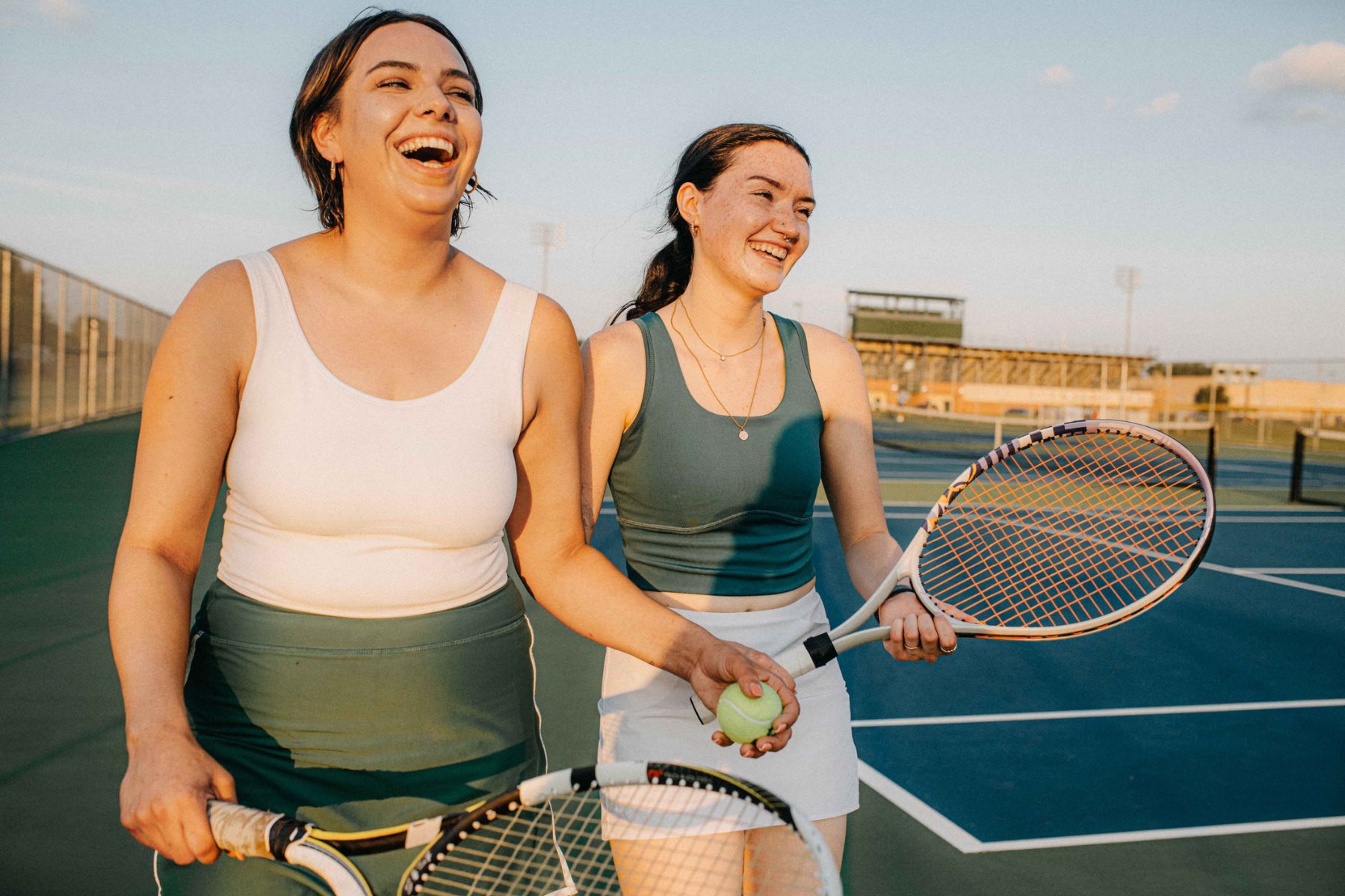 Two women in workout clothes holding a tennis ball and tennis rackets